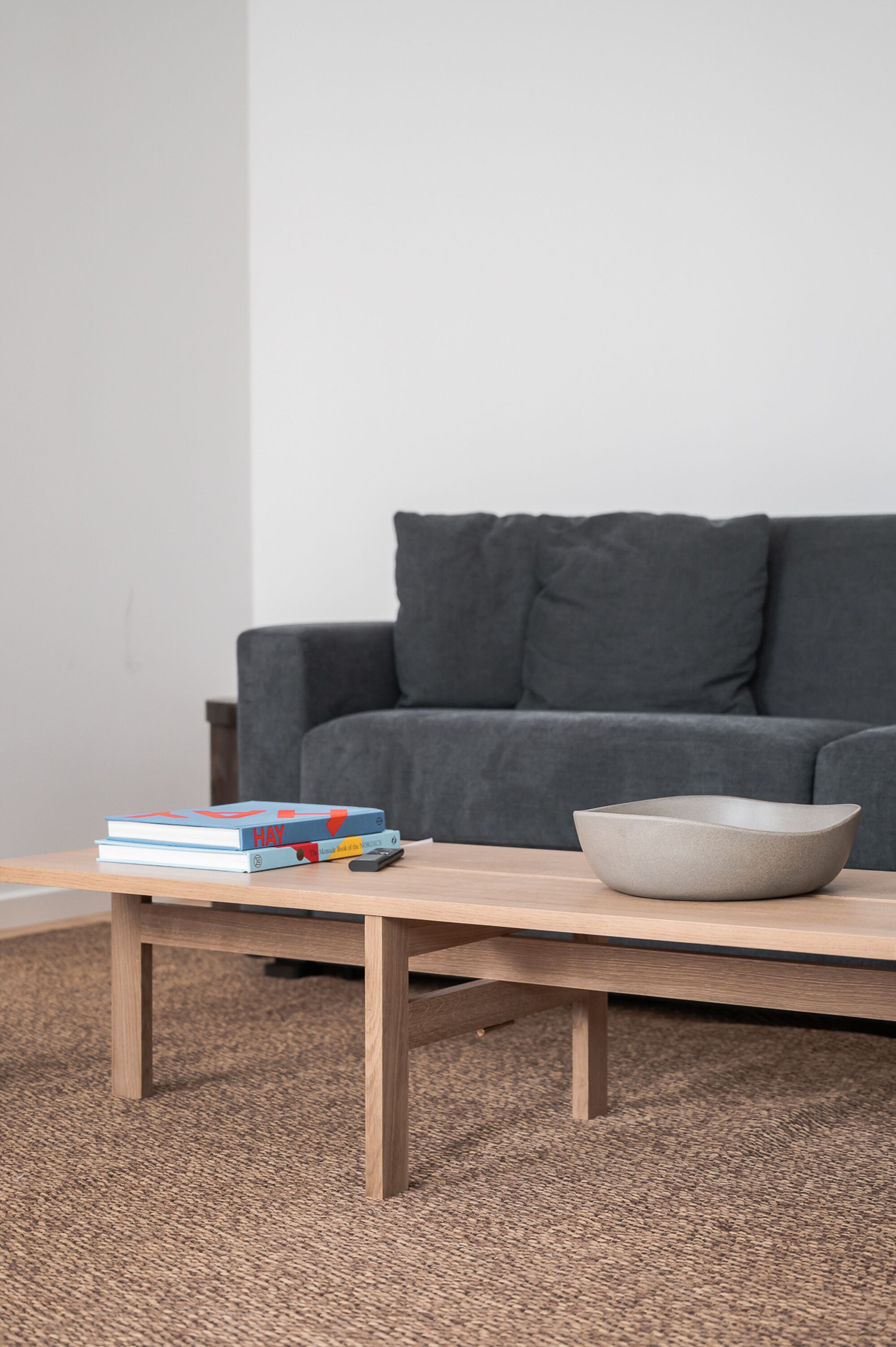 A modern living room with a grey sofa, a wooden coffee table, and a stack of books.