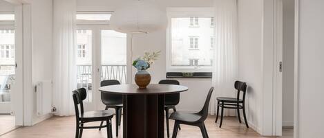 A dining area with a round table, black chairs, a vase with flowers, and a hanging light fixture.