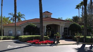 A building with a red-tiled roof, a wheelchair-accessible parking space, and a landscaped entrance area with red flowers and palm trees. - 4 Bdr/3Bath Home - 3mi to Disney - Heated pool/spa - No rear neighbors! (Kissimmee)