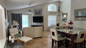 A living room with a sofa, a glass coffee table, a dining table with chairs, a TV, and a ceiling fan. - 4 Bdr/3Bath Home - 3mi to Disney - Heated pool/spa - No rear neighbors! (Kissimmee)