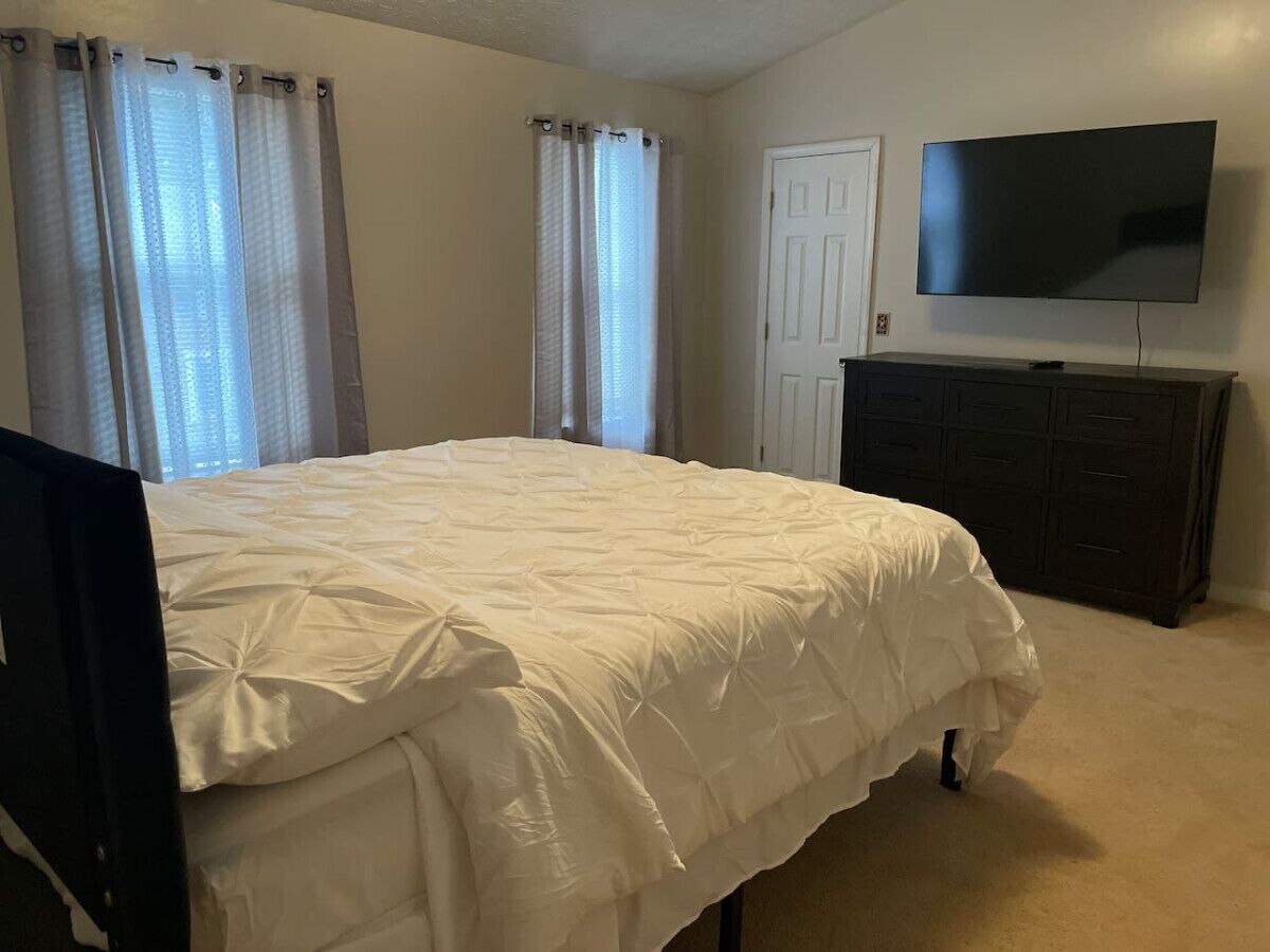 A bedroom with a bed, a TV, a dresser, and a door.