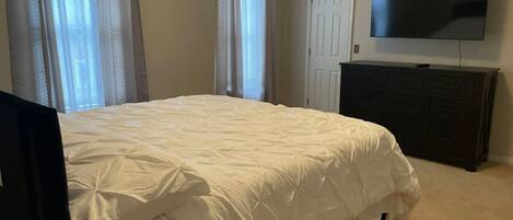A bedroom with a bed, a TV, a dresser, and a door.