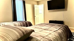A hotel room with two beds, a flat-screen TV mounted on the wall, and a door with a window. - Cozy 2BR Near Atlanta|Sleeps 5|Free Parking (Lithonia)