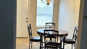 A dining area with a round table and four chairs, a chandelier, a window with blinds, and a door. - Cozy 2BR Near Atlanta|Sleeps 5|Free Parking (Lithonia)