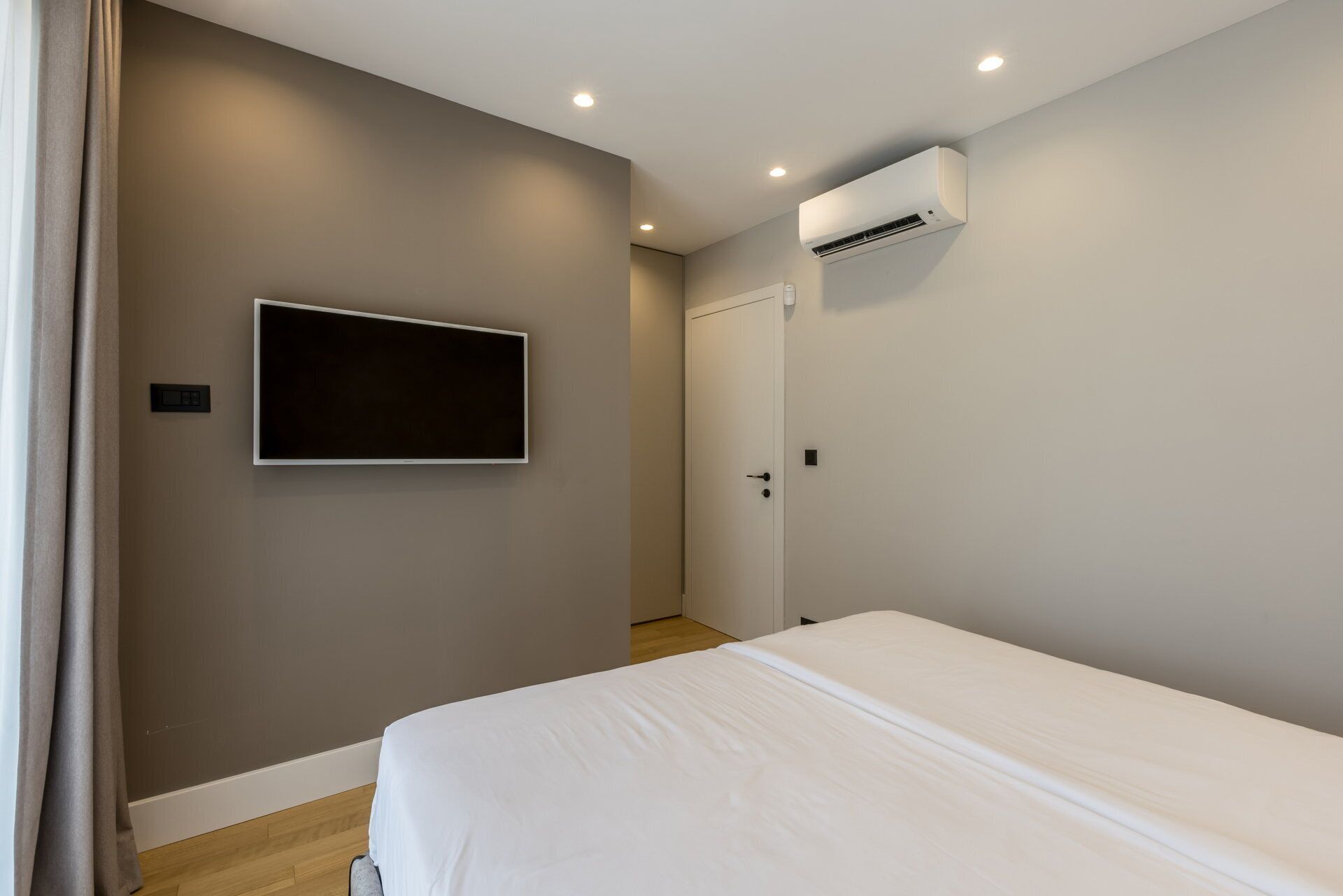 Une chambre à coucher comprenant un lit, un téléviseur fixé au mur, un appareil de climatisation et une porte.