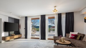 A modern living room with a flat-screen TV, a sofa, a coffee table, and a view of a mountainous landscape through large windows. - Villa Olivella with Heated Pool (Vodice)