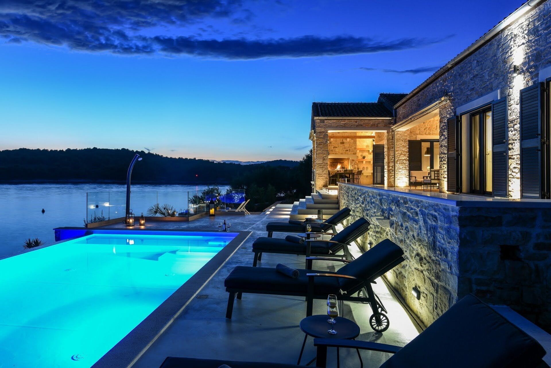 A poolside area with lounge chairs and a view of a lake at dusk.