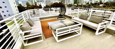 Un área de estar al aire libre con mobiliario blanco y vista a la ciudad.
