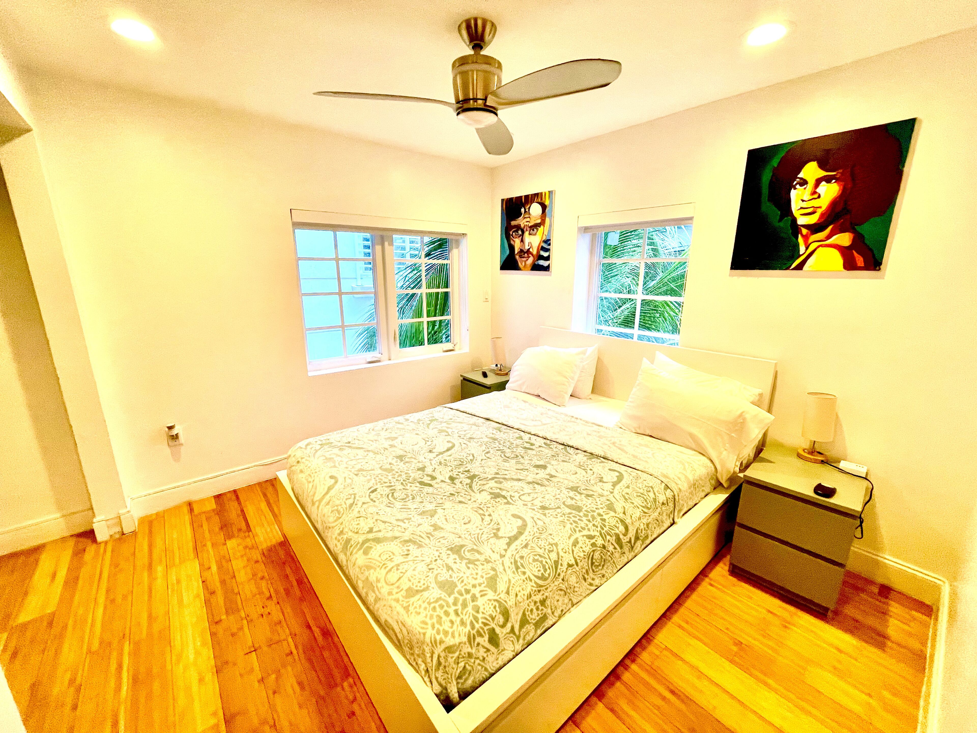 A bedroom with a bed, nightstands, a ceiling fan, and two windows.