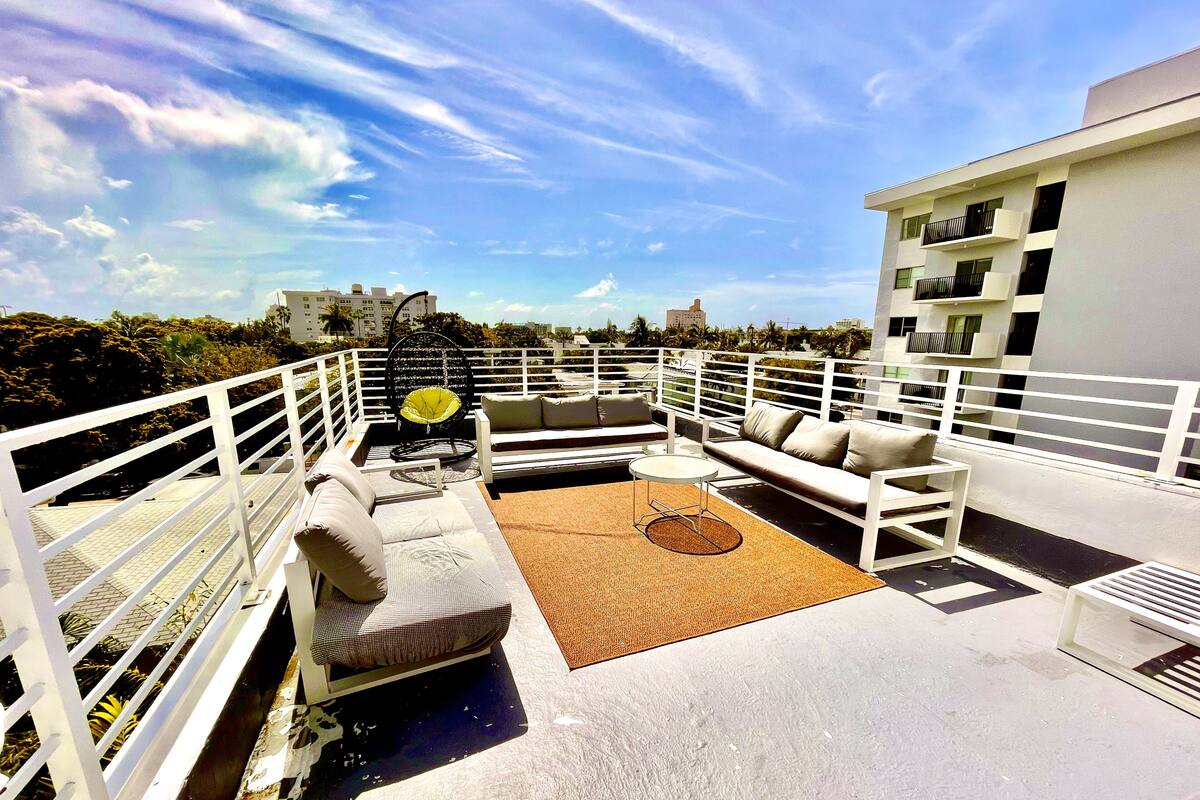 Una terraza en la azotea con barandilla blanca, un sofá, una silla y una mesita.