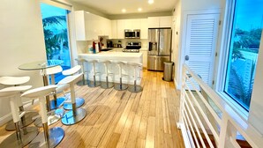 Une cuisine moderne avec des meubles blancs, des appareils en acier inoxydable et un coin bar équipé de tabourets.
