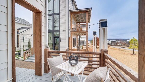 Une terrasse en bois avec une table blanche et deux chaises, donnant sur un quartier résidentiel avec des maisons et un ciel dégagé.