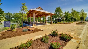 Un pavillon abrité, accessible par un sentier en pierre, entouré de jardins aménagés et d’arbres.