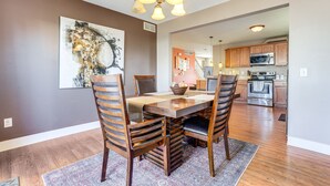 A dining area with a wooden table and chairs, a chandelier, and a large abstract painting on the wall. - Charming Kalamazoo Home w/ Yard: 1 Mi to Downtown! (Kalamazoo)