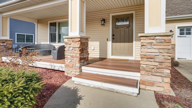 A house with a front porch, stone pillars, and a door with a window above it. - Charming Kalamazoo Home w/ Yard: 1 Mi to Downtown! (Kalamazoo)