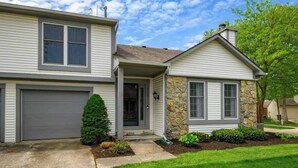 A two-story house with a garage, a stone facade, and a well-maintained lawn. - Family-Friendly 2BR Condo w/ Private Garage - Minutes from Zoo & Downtown (Fort Wayne)
