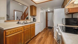 A compact kitchen with wooden cabinets, a white countertop, a built-in microwave, and a stove. - Family-Friendly 2BR Condo w/ Private Garage - Minutes from Zoo & Downtown (Fort Wayne)
