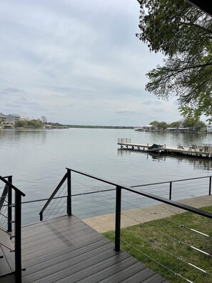 Un muelle de madera con barandilla da vista a un lago tranquilo, rodeado de casas y un embarcadero.
