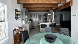 A modern kitchen with wooden beams, a central island, and a dining area with a glass table. - Spacious 6-bedroom house on Lake LB J (Granite Shoals)