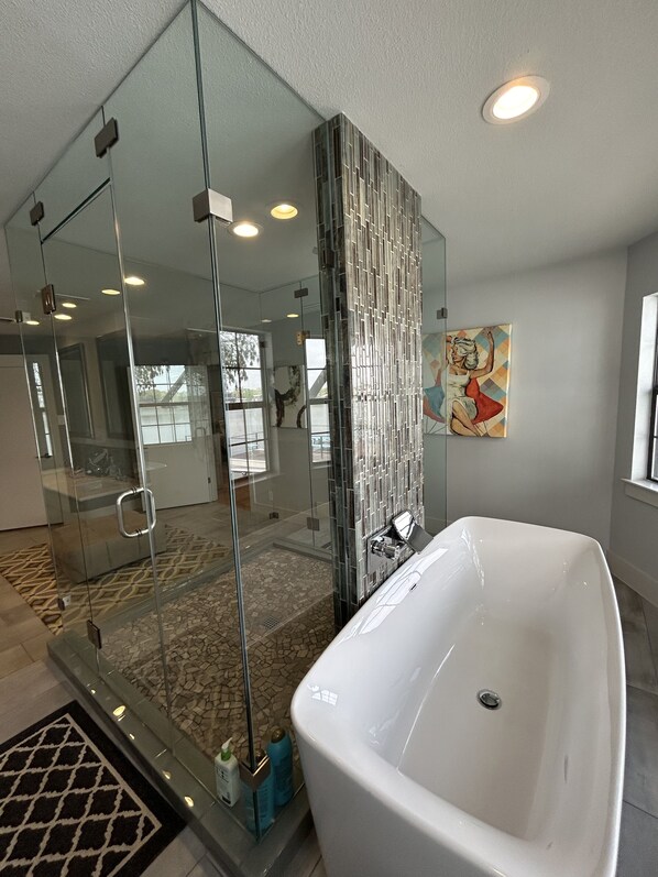 Un baño moderno con ducha de vidrio, bañera independiente y piso cubierto de azulejos.