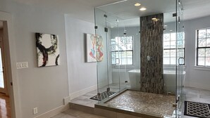 A modern bathroom with a glass shower enclosure, a large mirror, and a beige cushioned bench. - Spacious 6-bedroom house on Lake LB J (Granite Shoals)