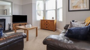 A living room with a television, wooden cabinet, and leather sofa. - The Mordon (Newquay)