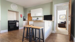 A compact kitchen with a microwave, oven, and wooden stools. - The Mordon (Newquay)