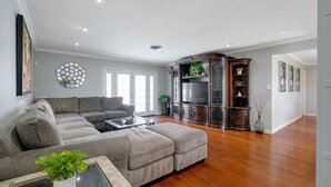 Un salon spacieux avec un canapé d’angle, un téléviseur à écran plat et un meuble de rangement en bois foncé.