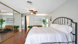 Une chambre avec un grand lit, un ventilateur de plafond et un miroir.