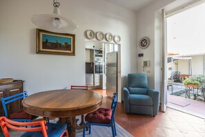A dining area with a wooden table and chairs, a blue armchair, and a kitchen with a refrigerator and microwave.