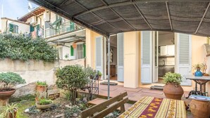 Eine überdachte Terrasse im Freien mit einer Holzbank, Topfpflanzen und einem gefliesten Boden.