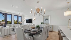A spacious living room with a large dining table, comfortable seating, a chandelier, and a TV. - Luxury Condo Overlooking Downtown Fairhope #301 (Fairhope)