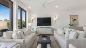 A modern living room with two sofas, a coffee table, a TV, and a ceiling fan. - Luxury Condo Overlooking Downtown Fairhope #301 (Fairhope)