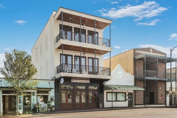 Un edificio de dos pisos con un balcón en el nivel superior, un letrero que dice 'Southern Tide' en la planta baja, y un letrero de 'First National Bank of Baldwin County' a la derecha.