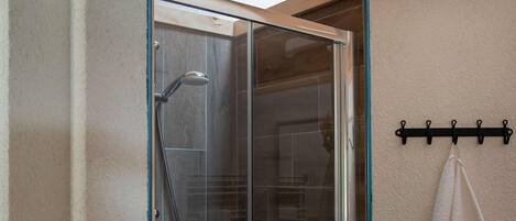 A glass-enclosed shower with a handheld showerhead, a towel rack with a towel, and a ceramic jar on a shelf above.