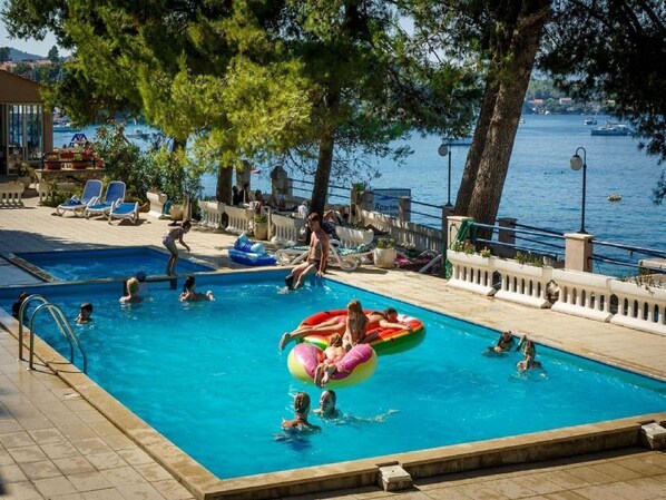 Relax by the pool surrounded by lounge chairs and a floating raft, with stunning views of the waterfront and boats.