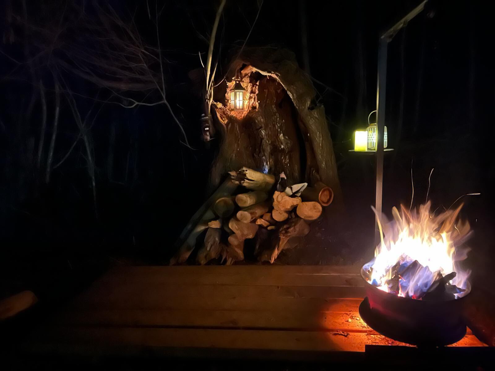 Un entorno rústico al aire libre con un banco de madera, un pequeño hogar para fuego y un farol.
