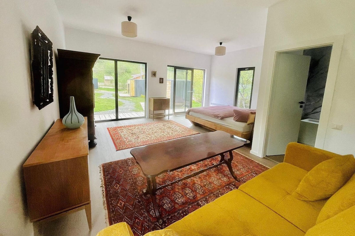 A spacious living area with a bed, a yellow sofa, a wooden coffee table, and a patterned rug.