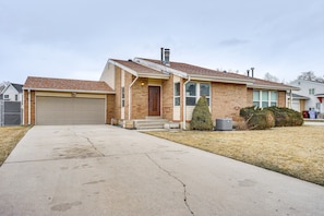 A single-story brick house with a garage, a front yard with a small tree, and a visible air conditioning unit. - Near 4 Major Ski Resorts: Salt Lake County Home (Midvale)