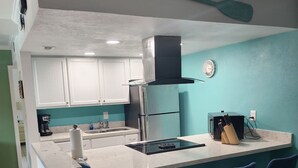 Een keuken met een centraal eiland, barkrukken, een koffieapparaat en een klok aan de muur.