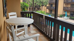 Een balkon met een witte tafel en stoelen, een betegelde vloer en uitzicht op een gebouw met balkons en bomen.