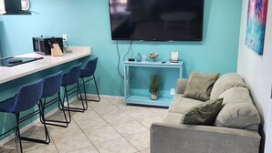Een compacte leefruimte met een kitchenette, een flatscreen-tv, een bank en een eethoek met stoelen.
