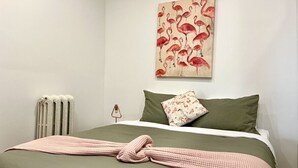 A bedroom with a bed, a radiator, a wall-mounted artwork of flamingos, and a green pillow. - The Flamingo ~ Cozy appartement in Saint-Roch - Downtown Quebec (Québec)