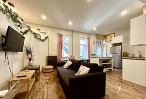 Ein modernes Wohnzimmer mit Sofa, Fernseher und einer Küchenzeile im Hintergrund.