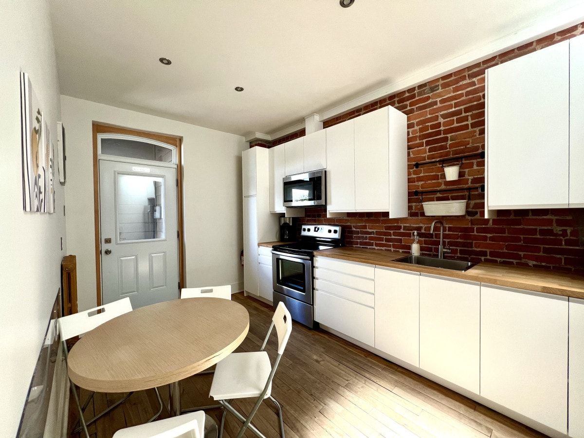 Cocina compacta con armarios blancos, microondas, horno y pileta.