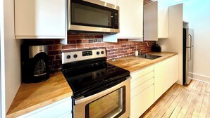 A modern kitchen with white cabinets, a stainless steel microwave, a black stove, and a built-in oven. - L'Ananas ~ A Charming Home in the Heart of Downtown (Québec)
