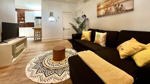 A living room with a black sofa, a television, a patterned rug, and a painting on the wall. - L'Ananas ~ A Charming Home in the Heart of Downtown (Québec)