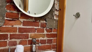 Un baño con un lavamanos blanco, un espejo redondo y una pared de ladrillo.