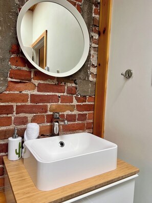 A bathroom with a white sink, a round mirror, and a brick wall. - Le Cactus ~ A Stunning Home in the St-Roch Neighborhood (Québec)