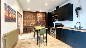 A modern kitchen with a brick wall, wooden dining table, and black cabinets. - The Cactus ~ Superb accomodation in Saint-Roch, Downtown Quebec (Québec)
